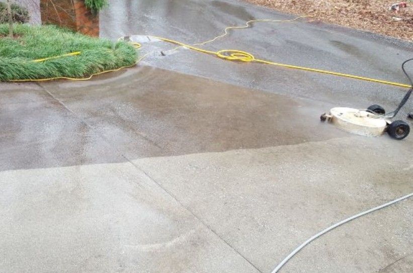 A concrete driveway is being cleaned with a pressure washer.