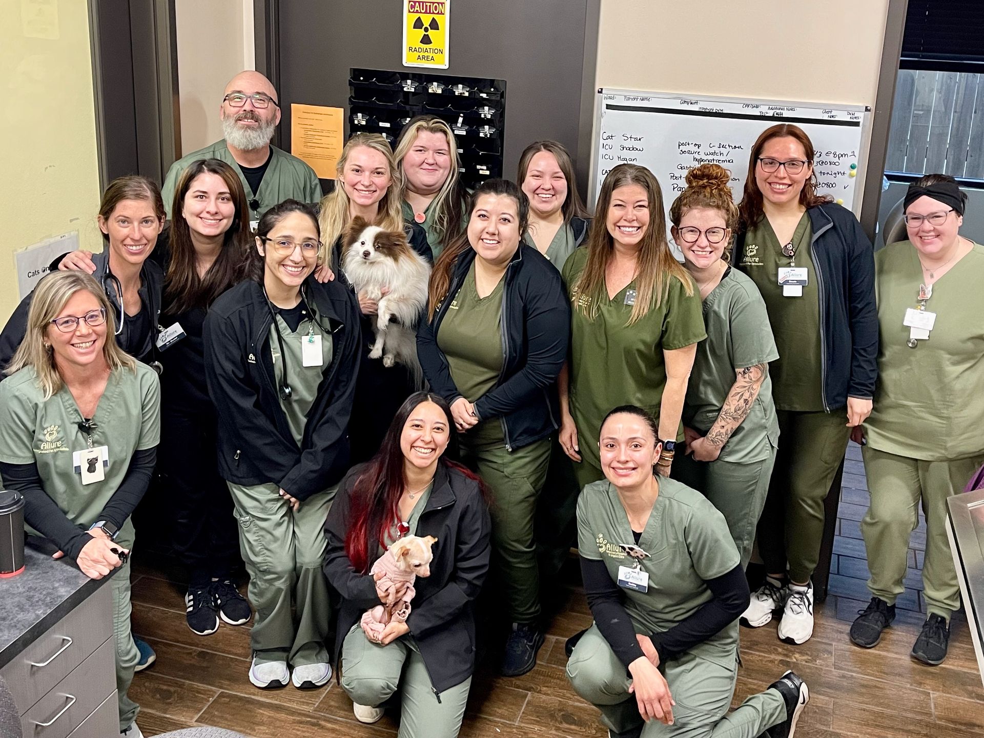 Group of people in green scrubs posing with pets in a veterinary office.