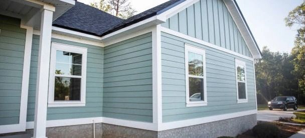 A light blue house with white trim, windows, and dark roof. A car is parked on the street.