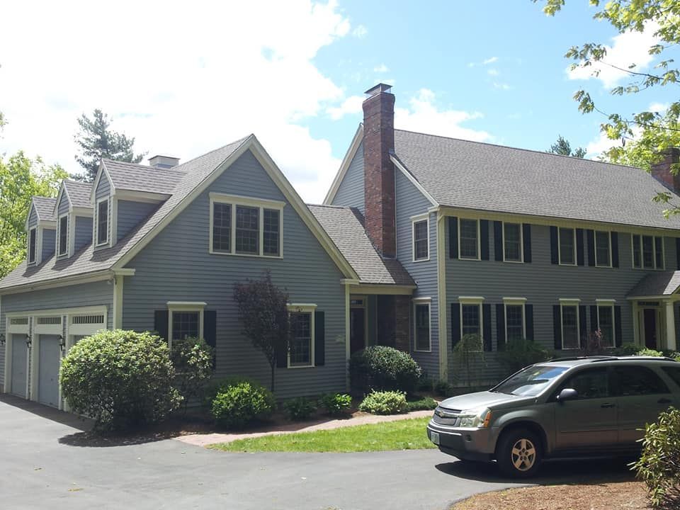 Blue house with three-car garage, multiple windows, gray roof, black shutters, and silver SUV in the driveway.