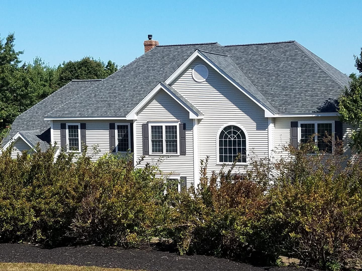 White house with gray roof, surrounded by bushes, with blue sky.