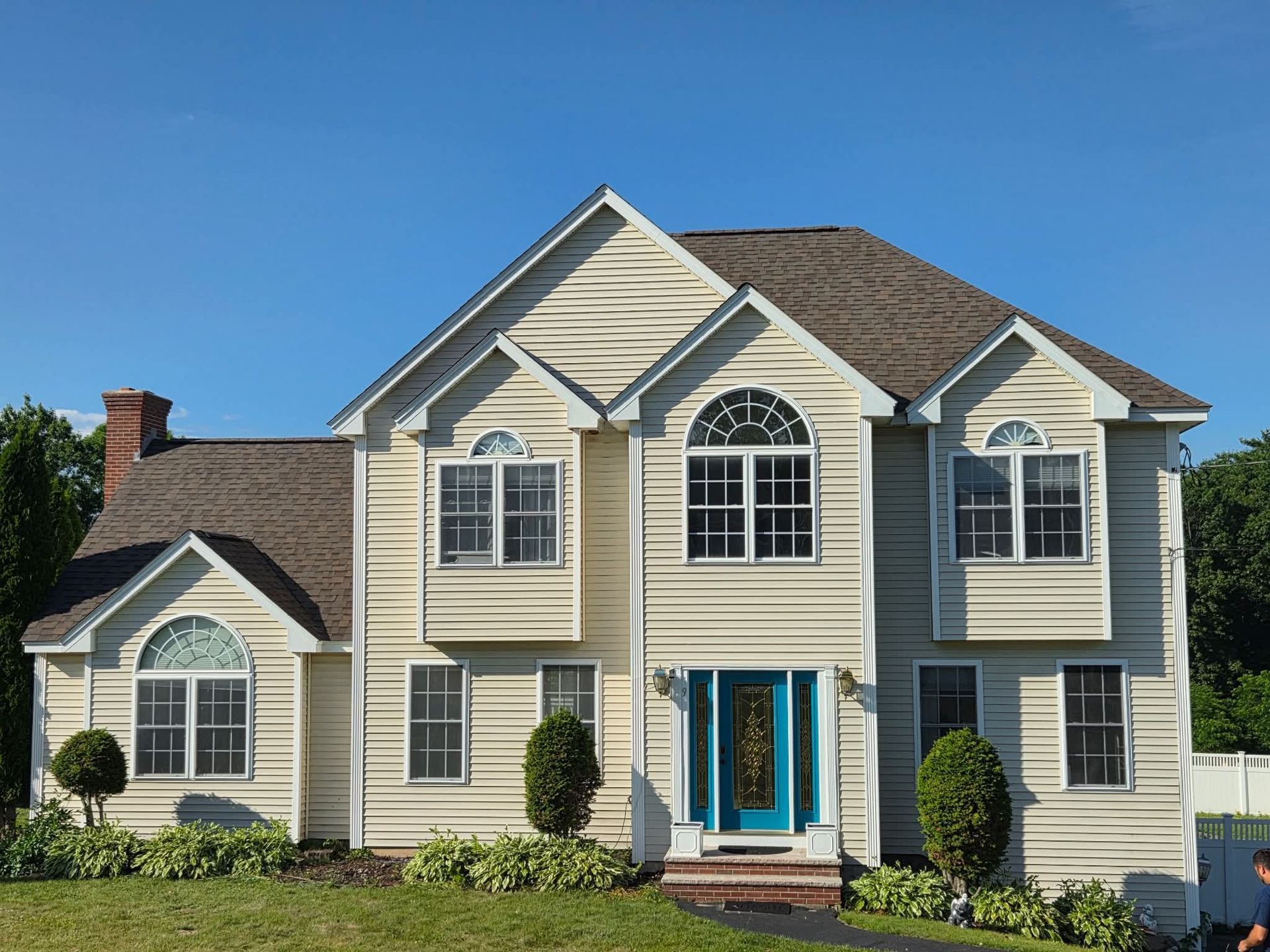 Suburban two-story beige house with white trim, black shutters, and a bright blue front door