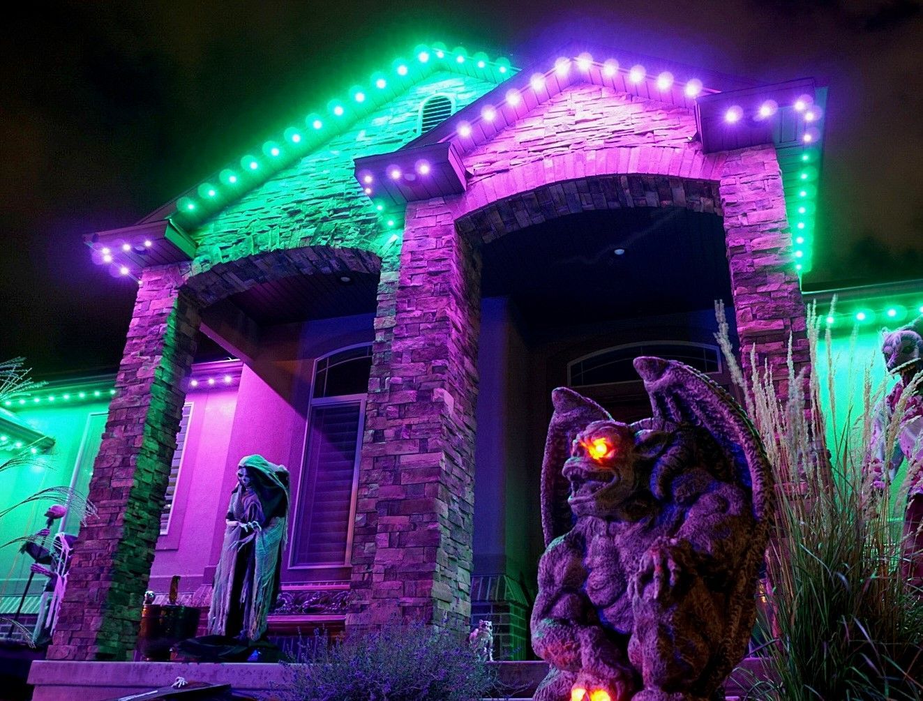 A house decorated for halloween with purple and green lights and a gargoyle statue.