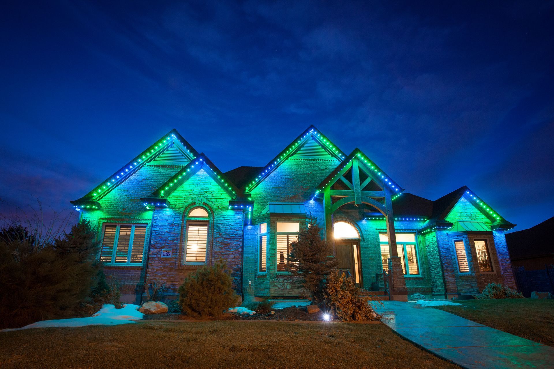 A large brick house is decorated with blue and green christmas lights.