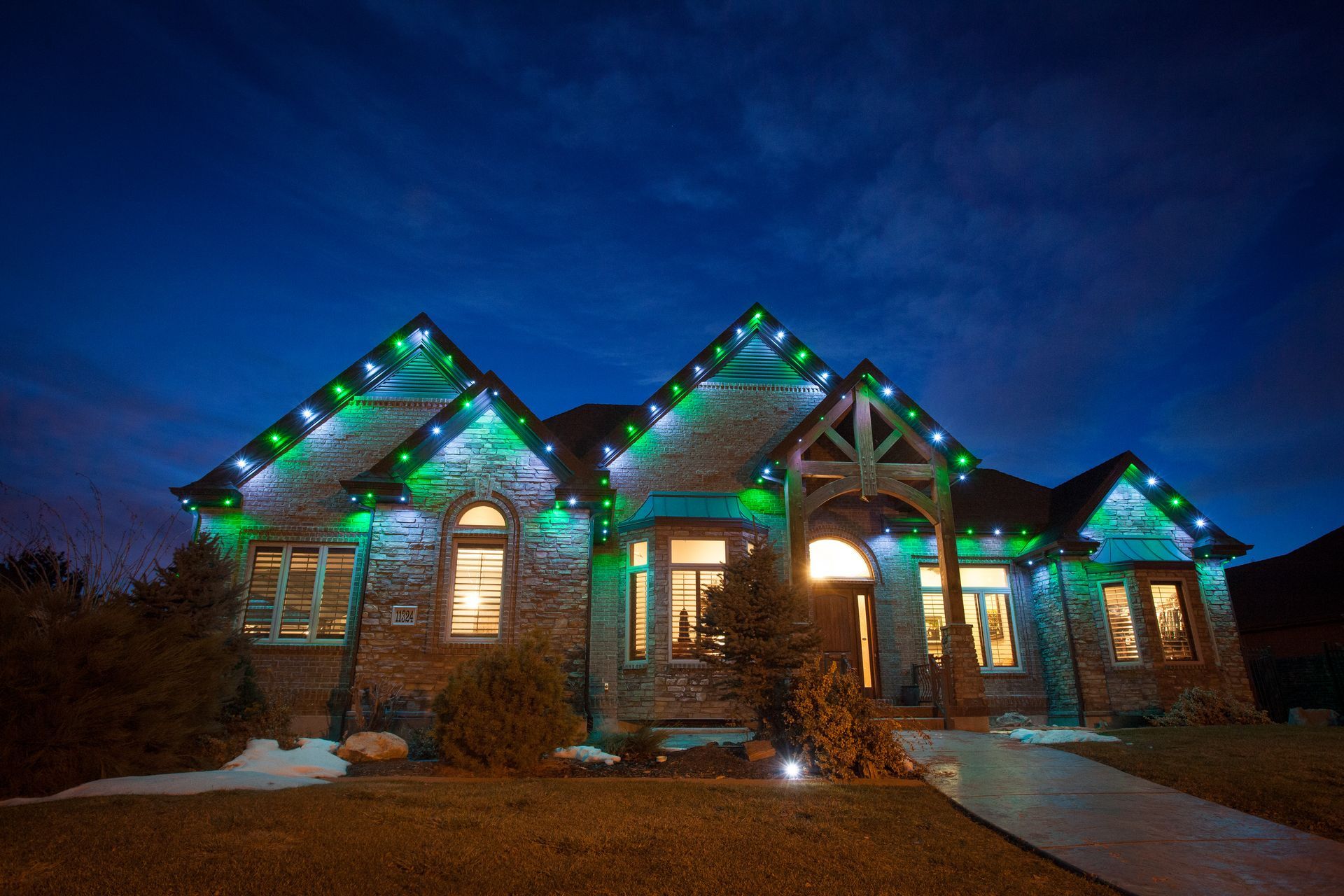 A large brick house decorated with green christmas lights at night.