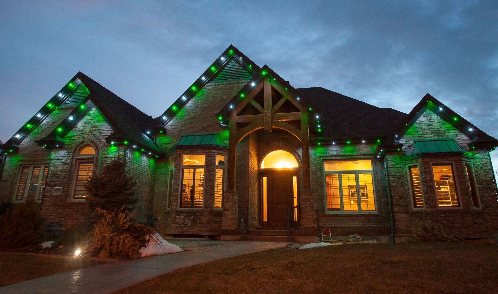 A large brick house is decorated with green christmas lights.