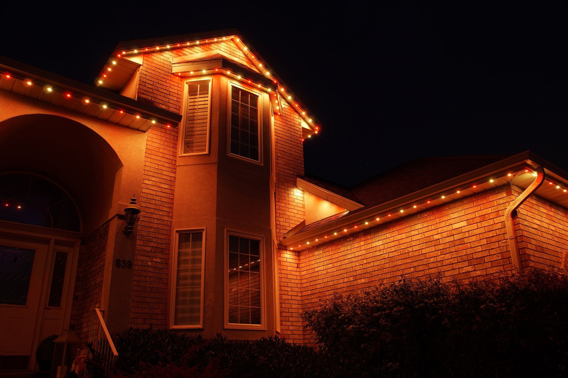 A large brick house is lit up with christmas lights at night