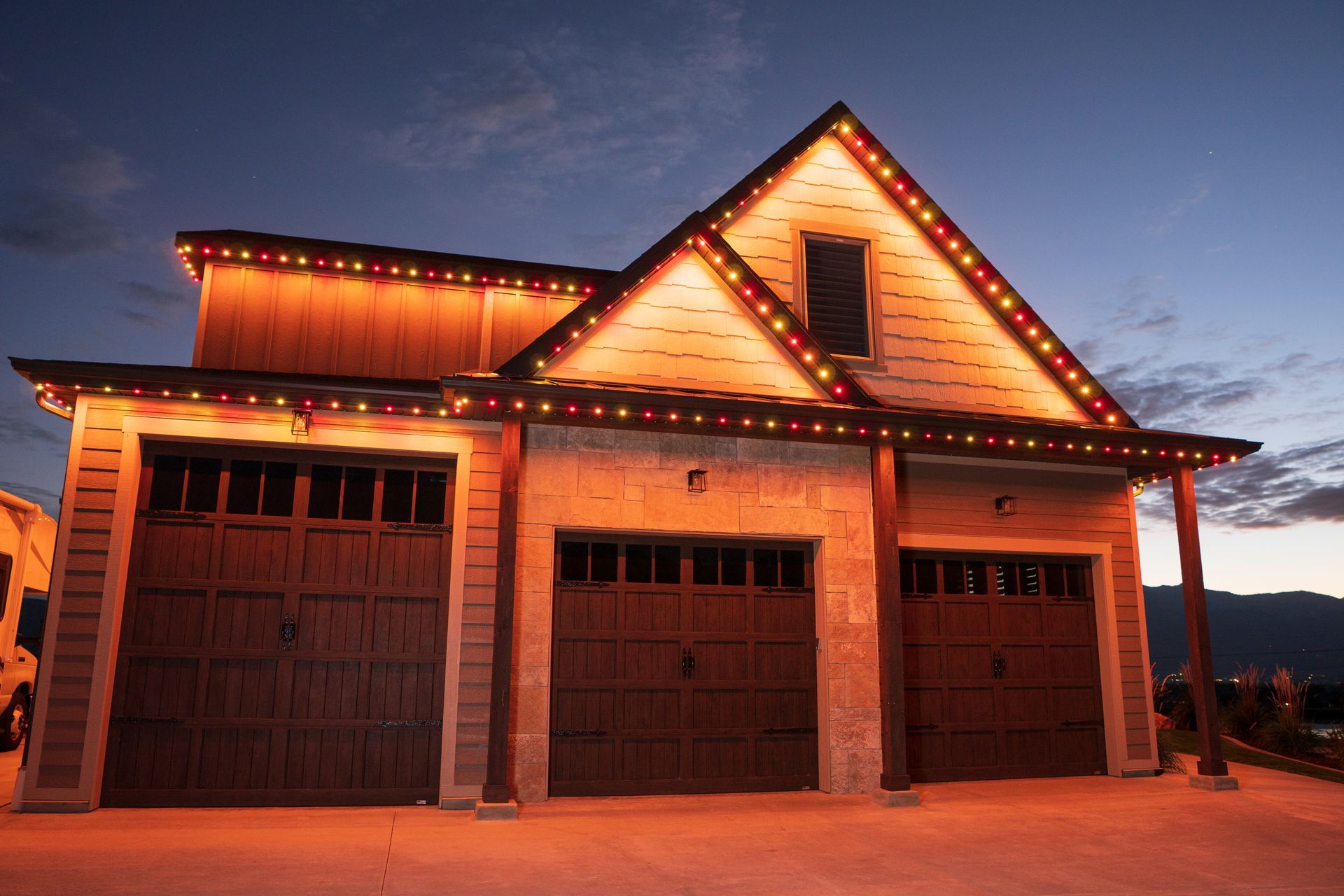 A large house with three garage doors is decorated with christmas lights.