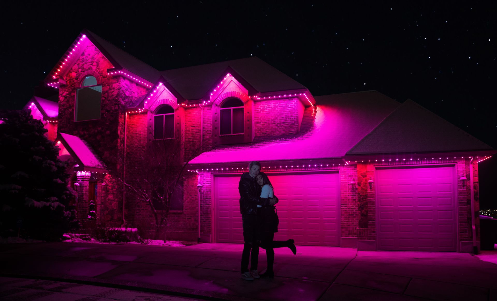 A couple is standing in front of a house with pink lights on it.