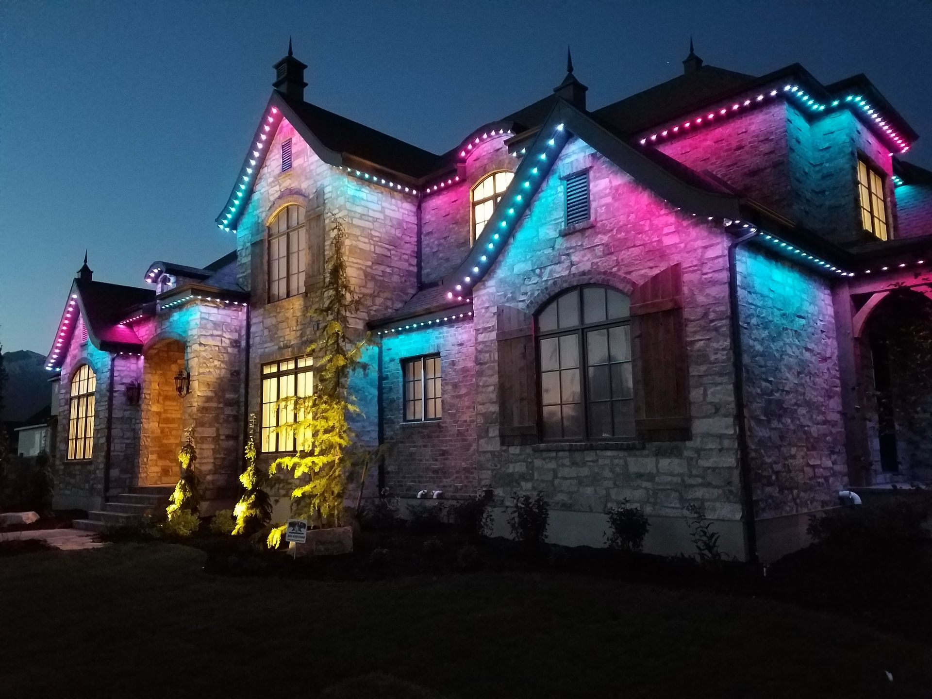 A large brick house is decorated with christmas lights at night.