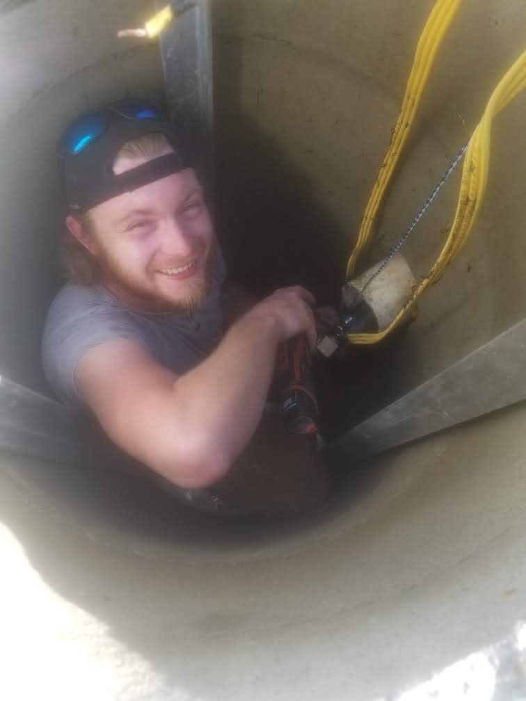 A man is sitting in a hole with a yellow rope.