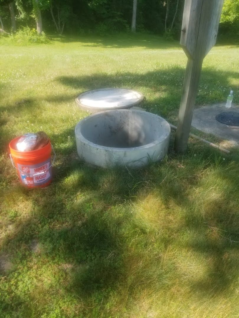 A bucket is sitting next to a septic tank in the grass.