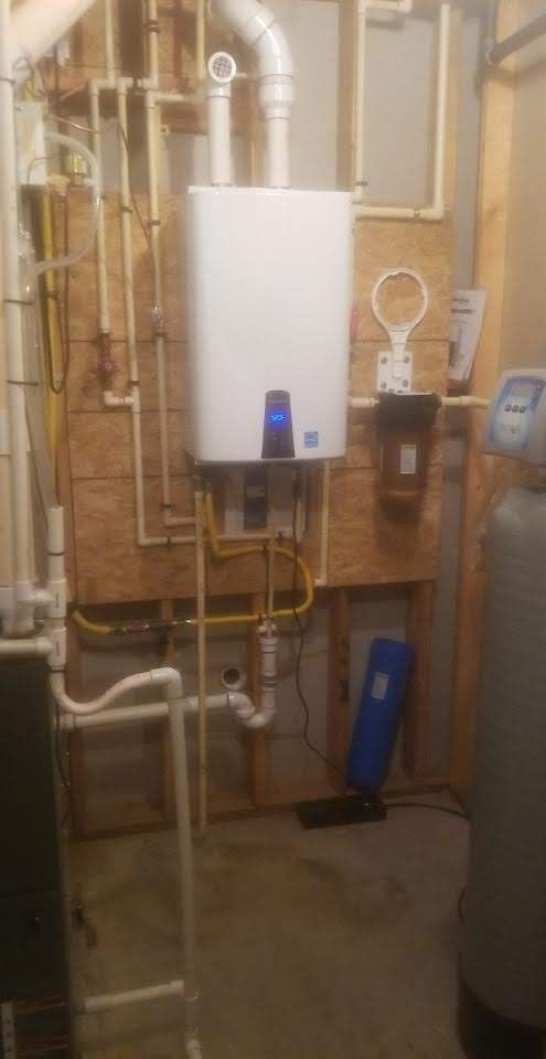 A white boiler is sitting in a basement next to a water tank.