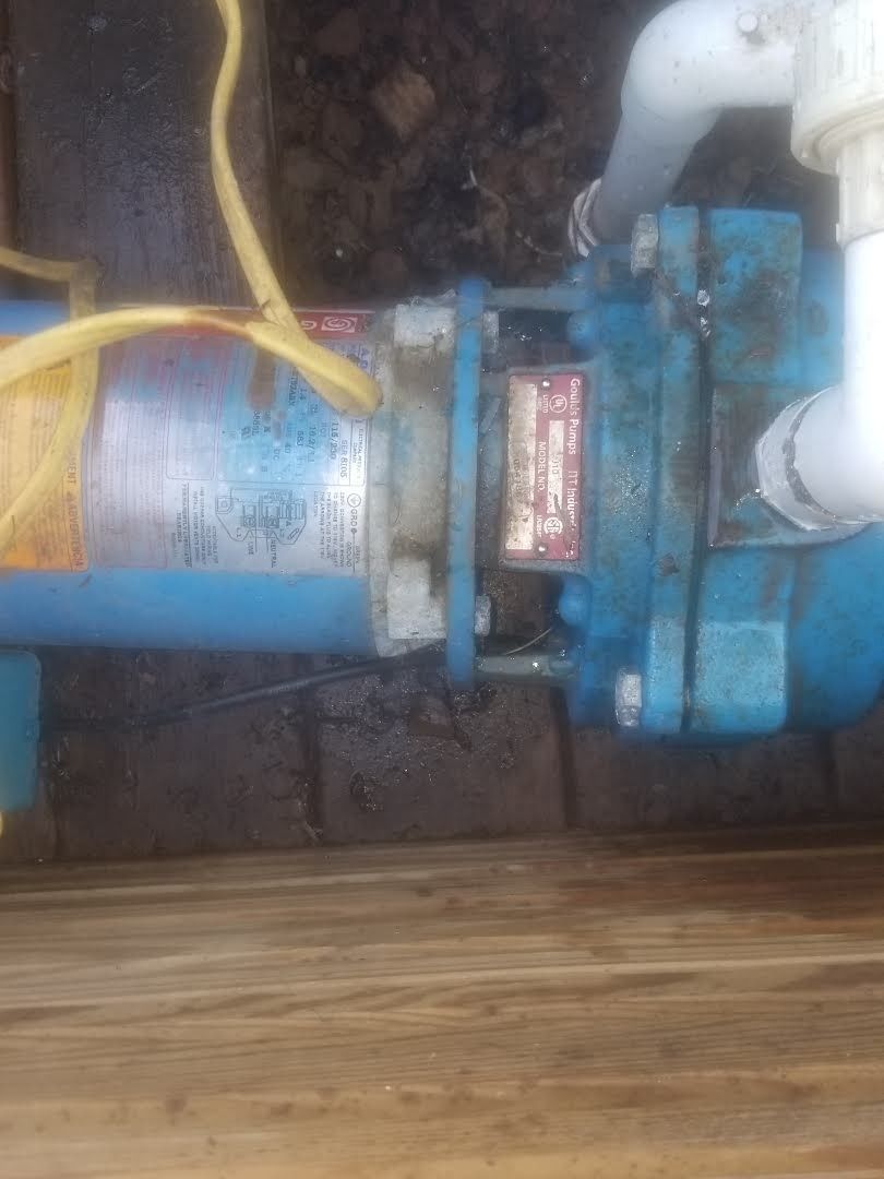 A blue water pump is sitting on top of a wooden floor next to a pipe.