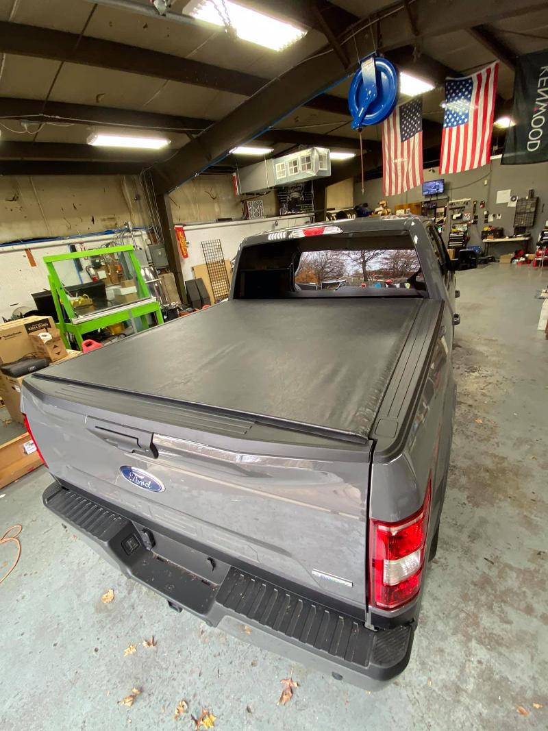 A gray truck with a black bed cover is parked in a garage.