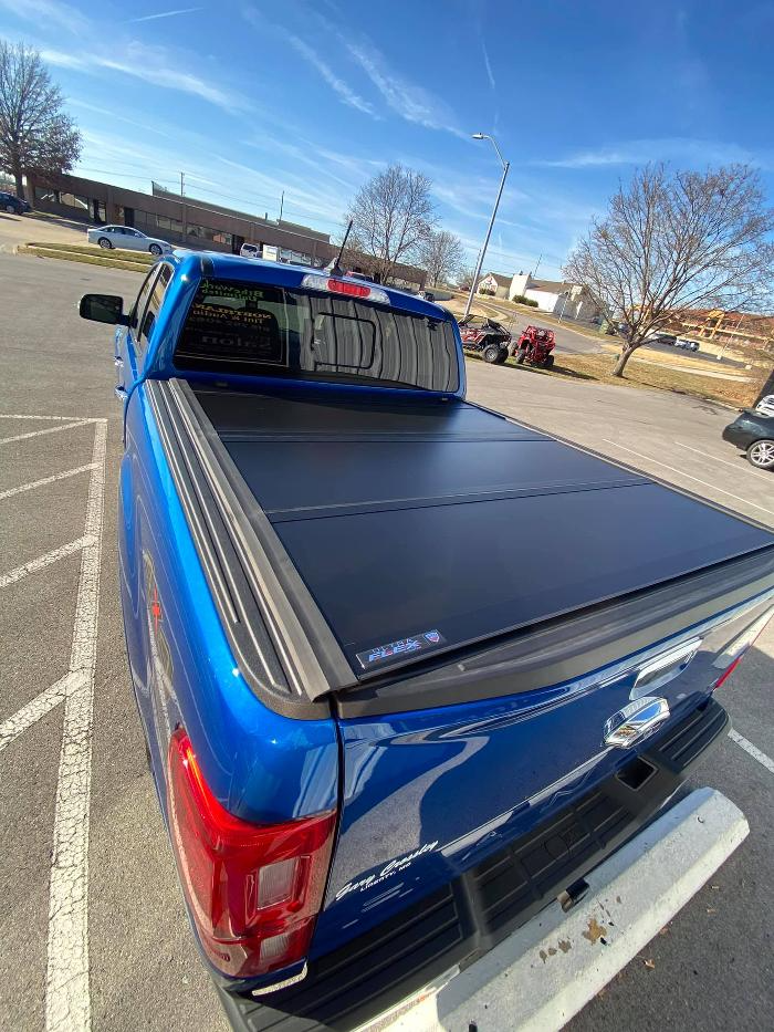 A blue truck with a black bed cover is parked in a parking lot.