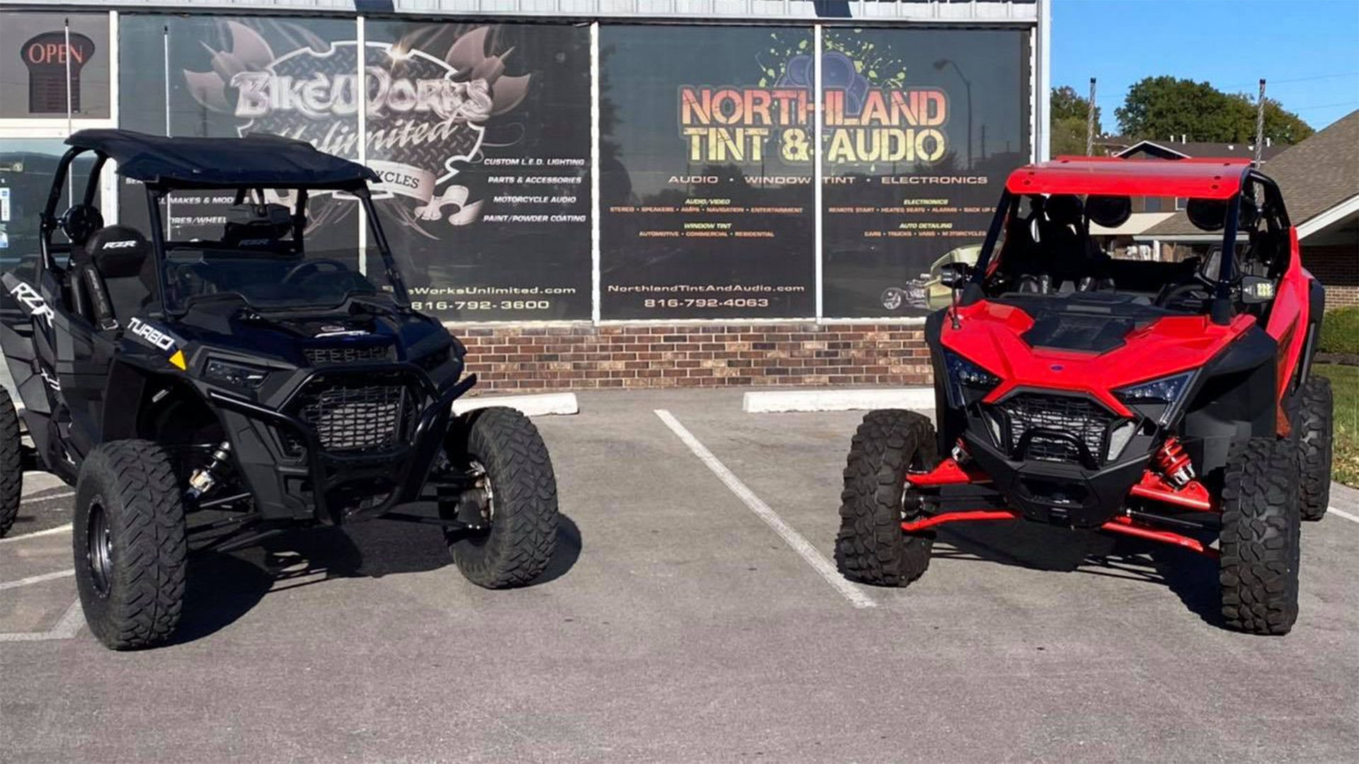 Two atvs are parked in a parking lot in front of a building.