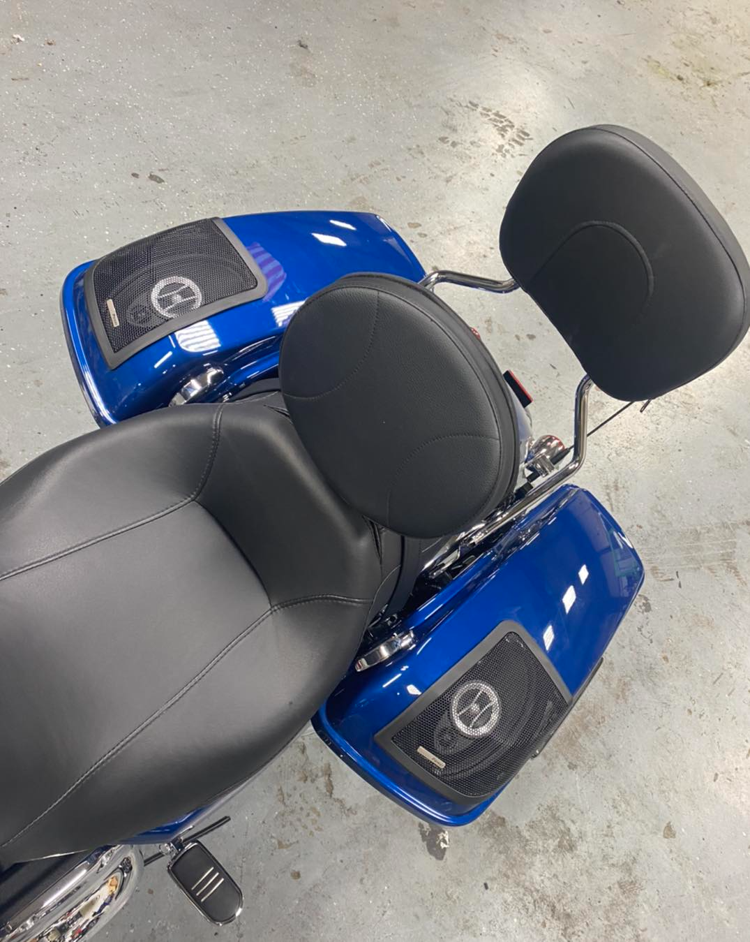 A blue motorcycle with black seats and speakers is sitting on a concrete floor.
