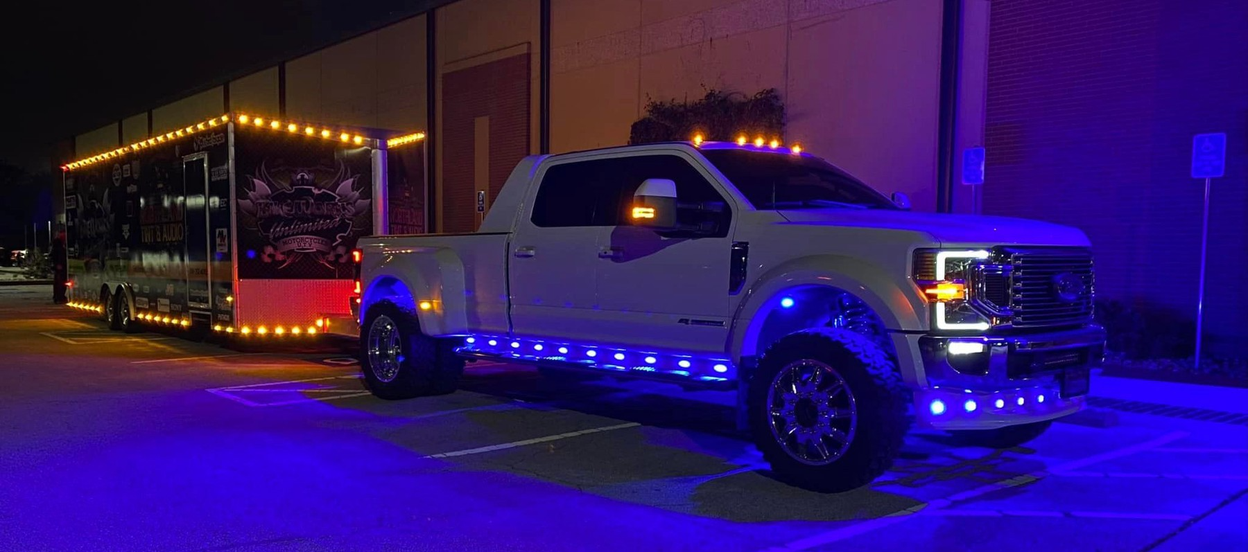 A white truck is parked in a parking lot next to a trailer.