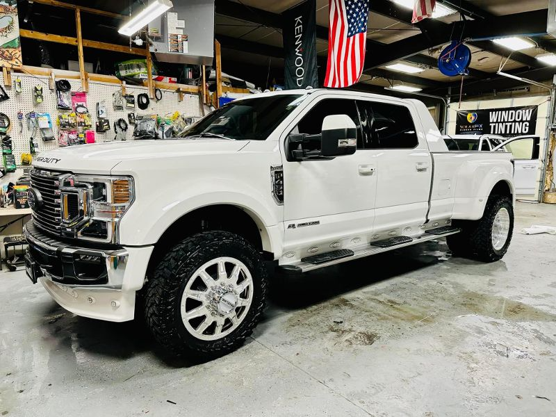 A white pickup truck is parked in a garage with an american flag hanging from the ceiling.