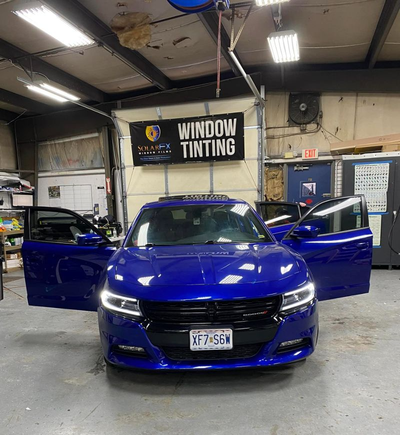 A blue car is parked in front of a window tinting sign