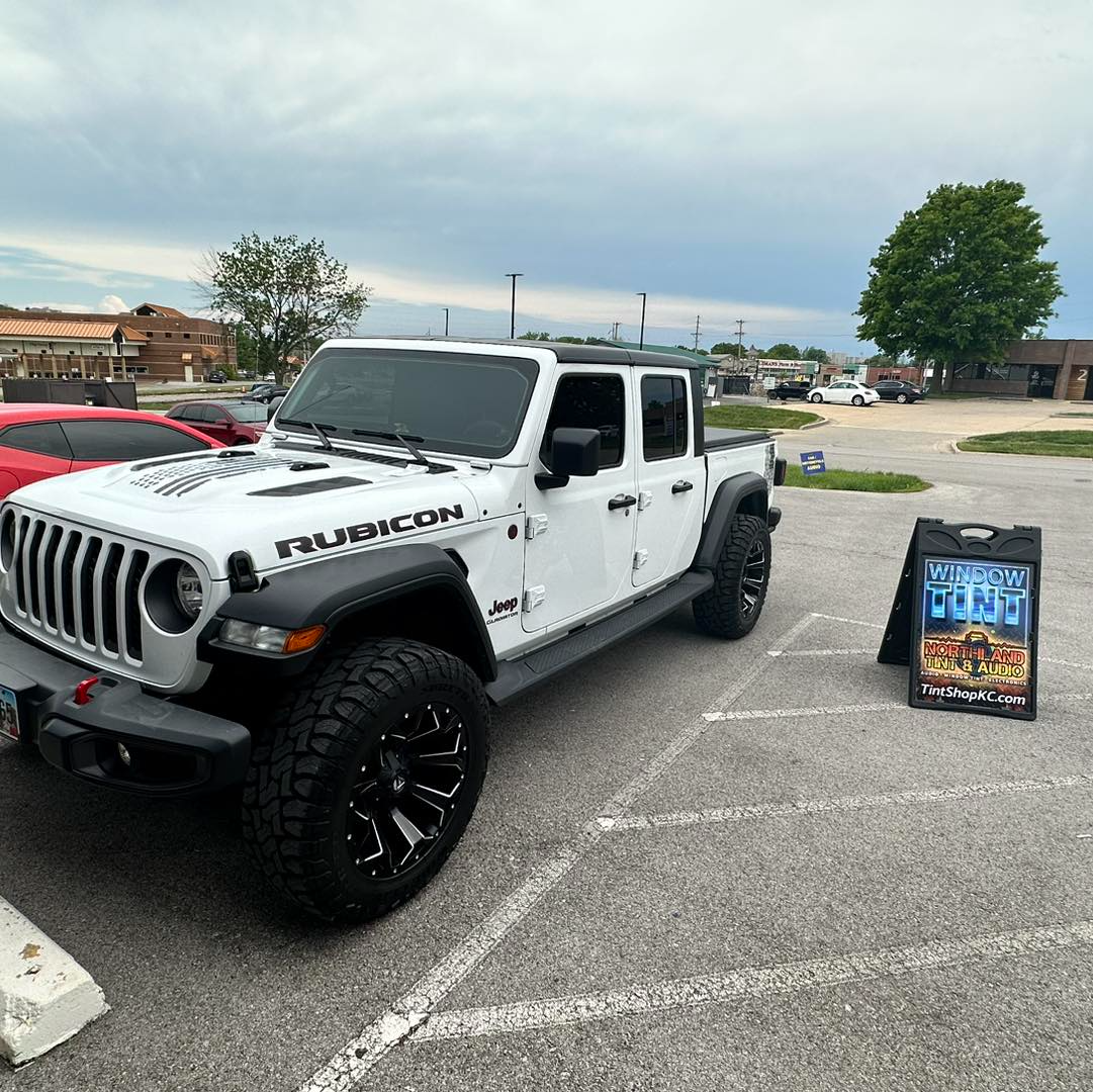 A white jeep is parked in a parking lot next to a sign.