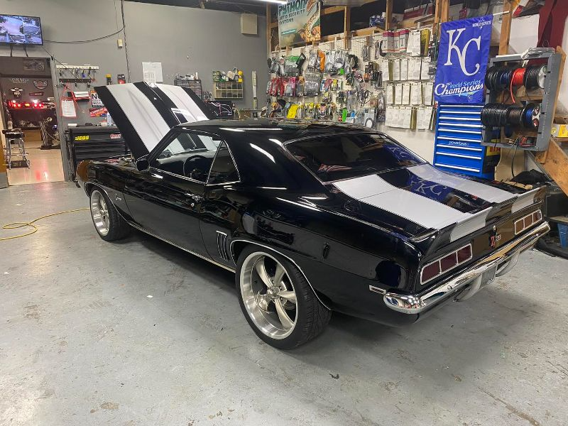 A black car with the hood up is parked in a garage.