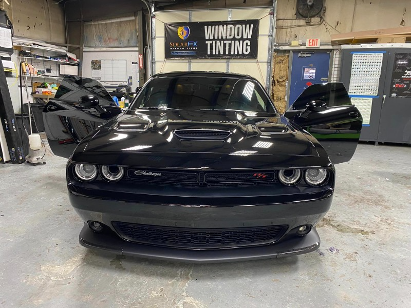 A black dodge challenger is parked in a garage with its doors open.