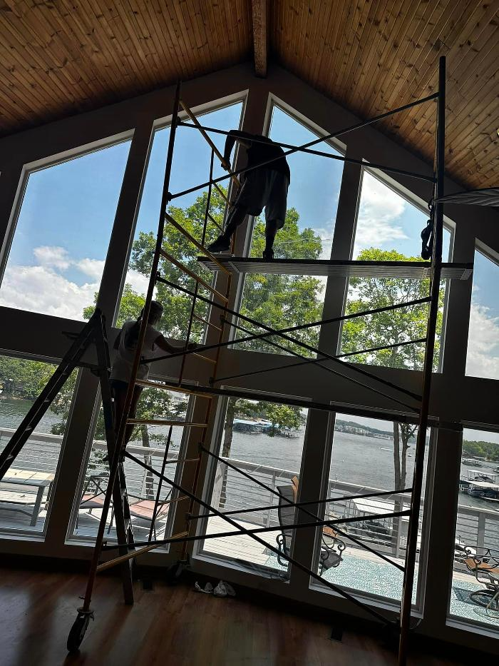 A man is standing on a scaffolding in front of a large window.