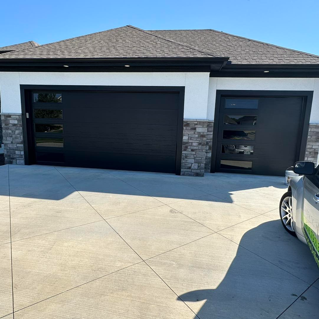 A car is parked in front of a house with black garage doors.