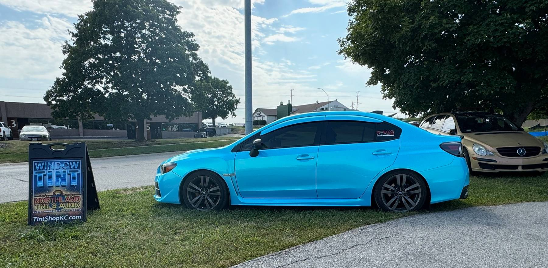 A blue car is parked on the side of the road next to a sign.