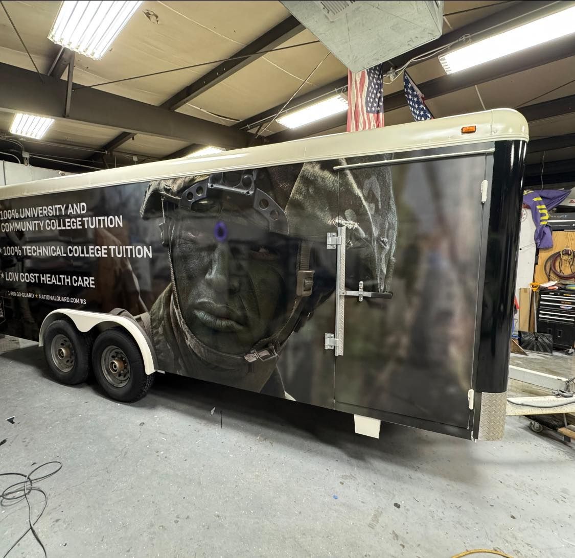 A trailer parked in a workshop features a large wrap showing a soldier in combat gear and military benefit text.