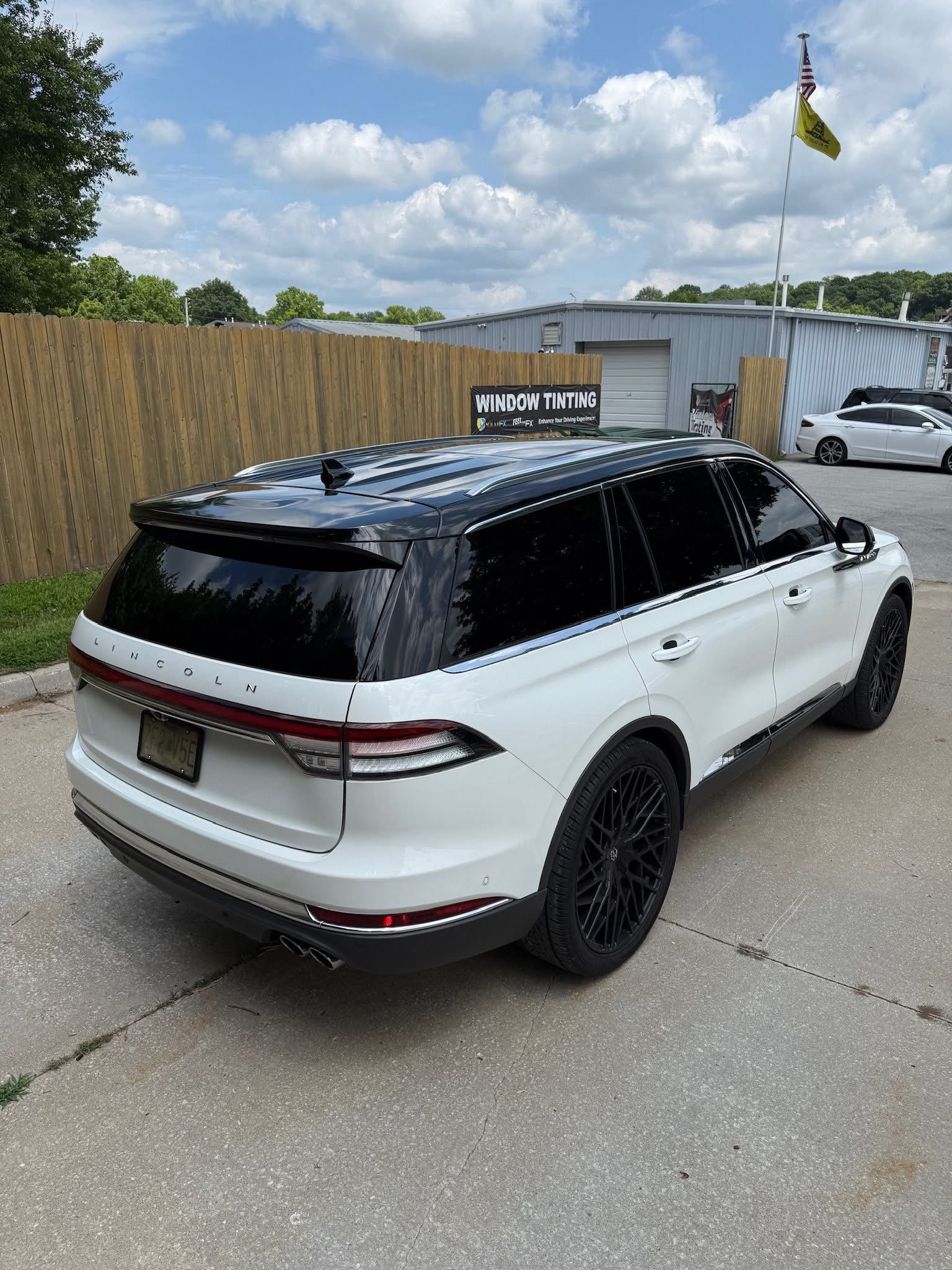 A white Lincoln Navigator SUV with a black roof and black wheels, parked on a paved lot in front of a building.