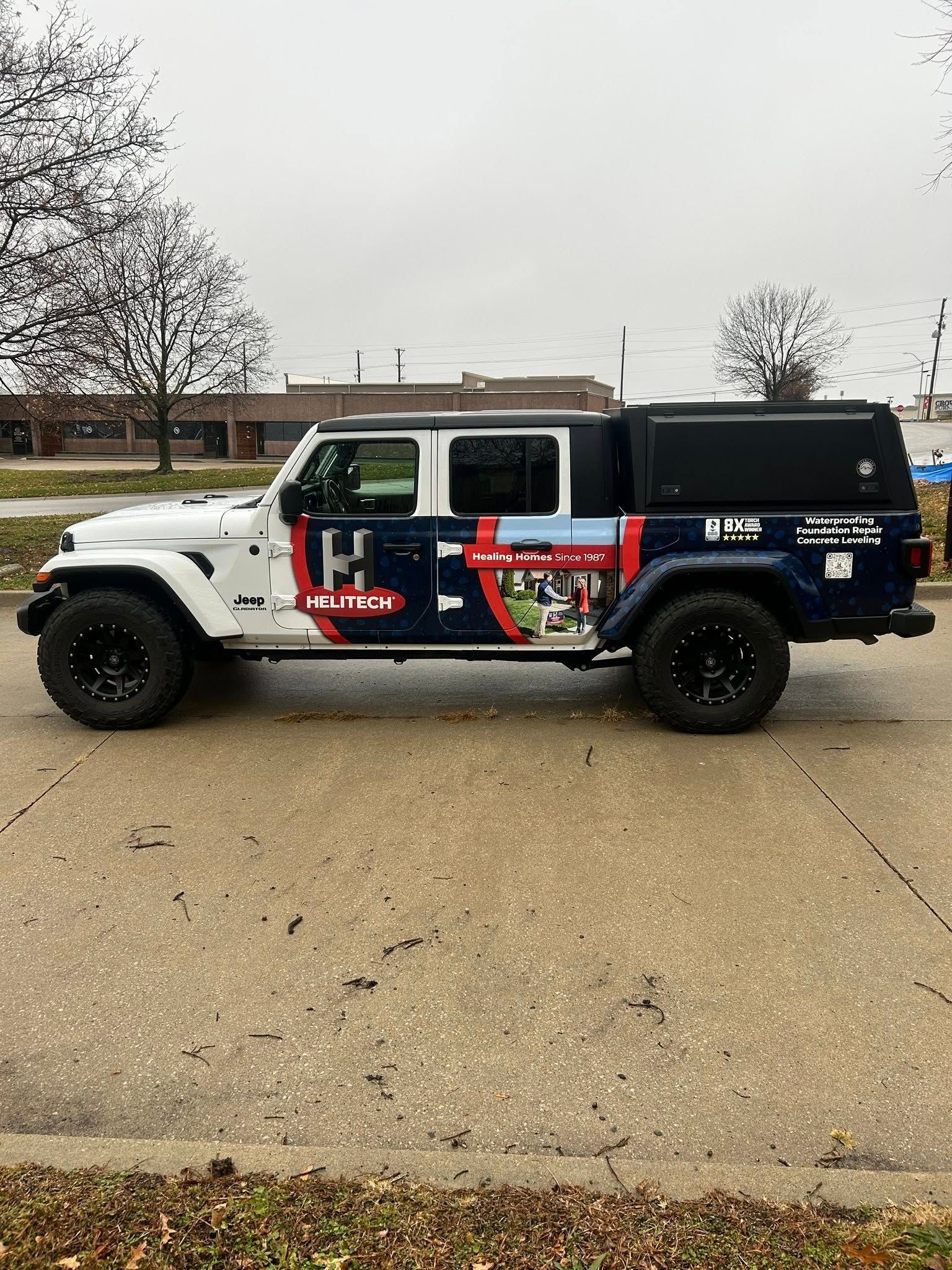 A white and dark blue Jeep Gladiator pickup truck with a black camper shell parked on a paved lot.