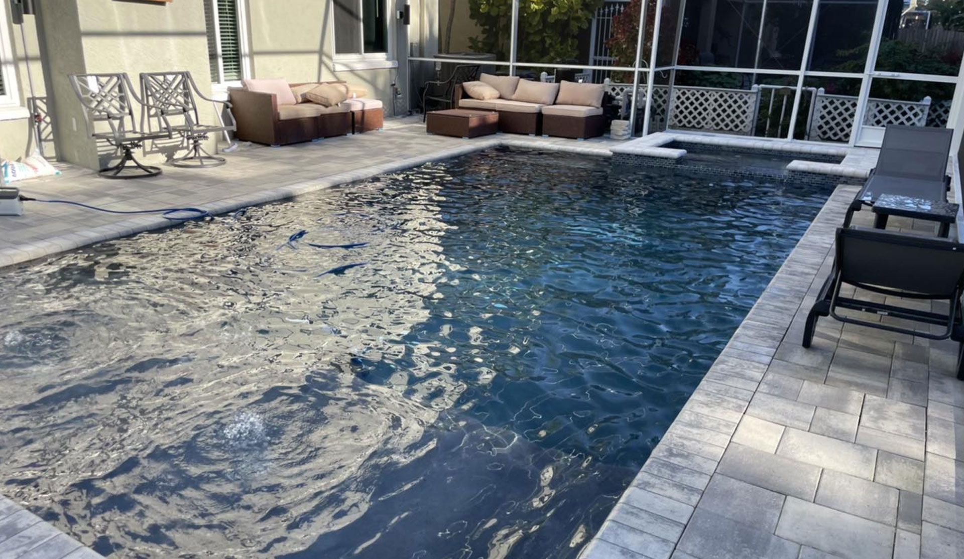 Swimming pool with lounge chairs, patio furniture, and surrounding screened enclosure.