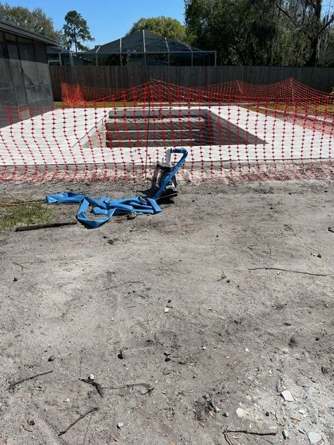 Newly constructed concrete pool area with safety fencing; blue straps on ground.