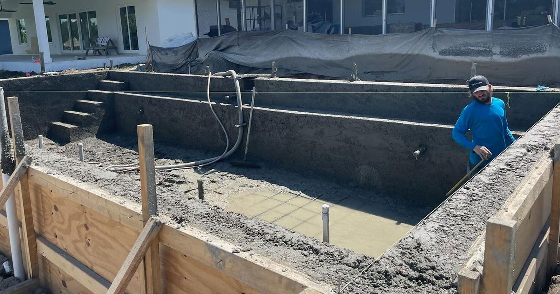 Pool under construction with cement walls and a worker in blue shirt.