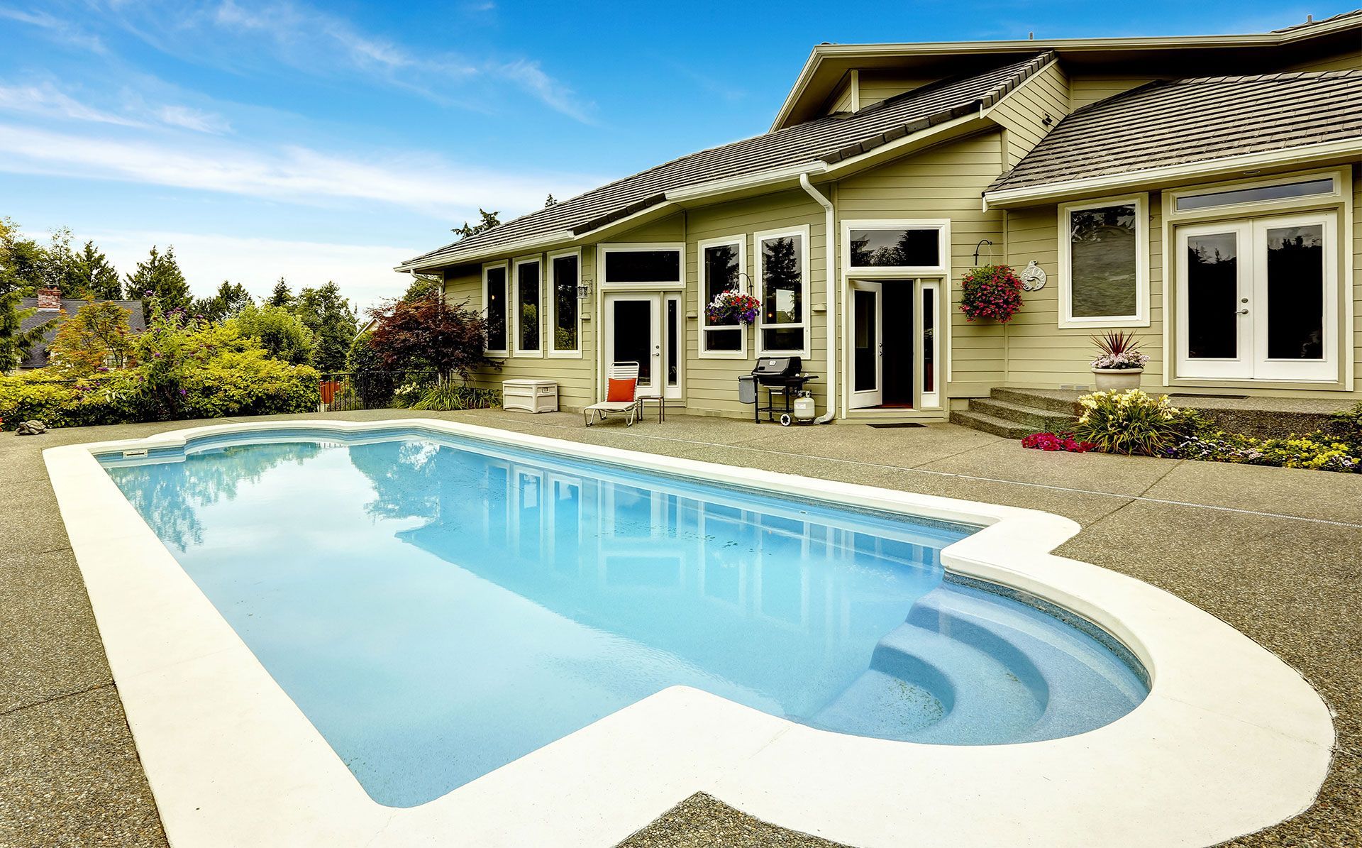 Pool in front of a beige house with multiple windows and doors, sunny outdoor setting.