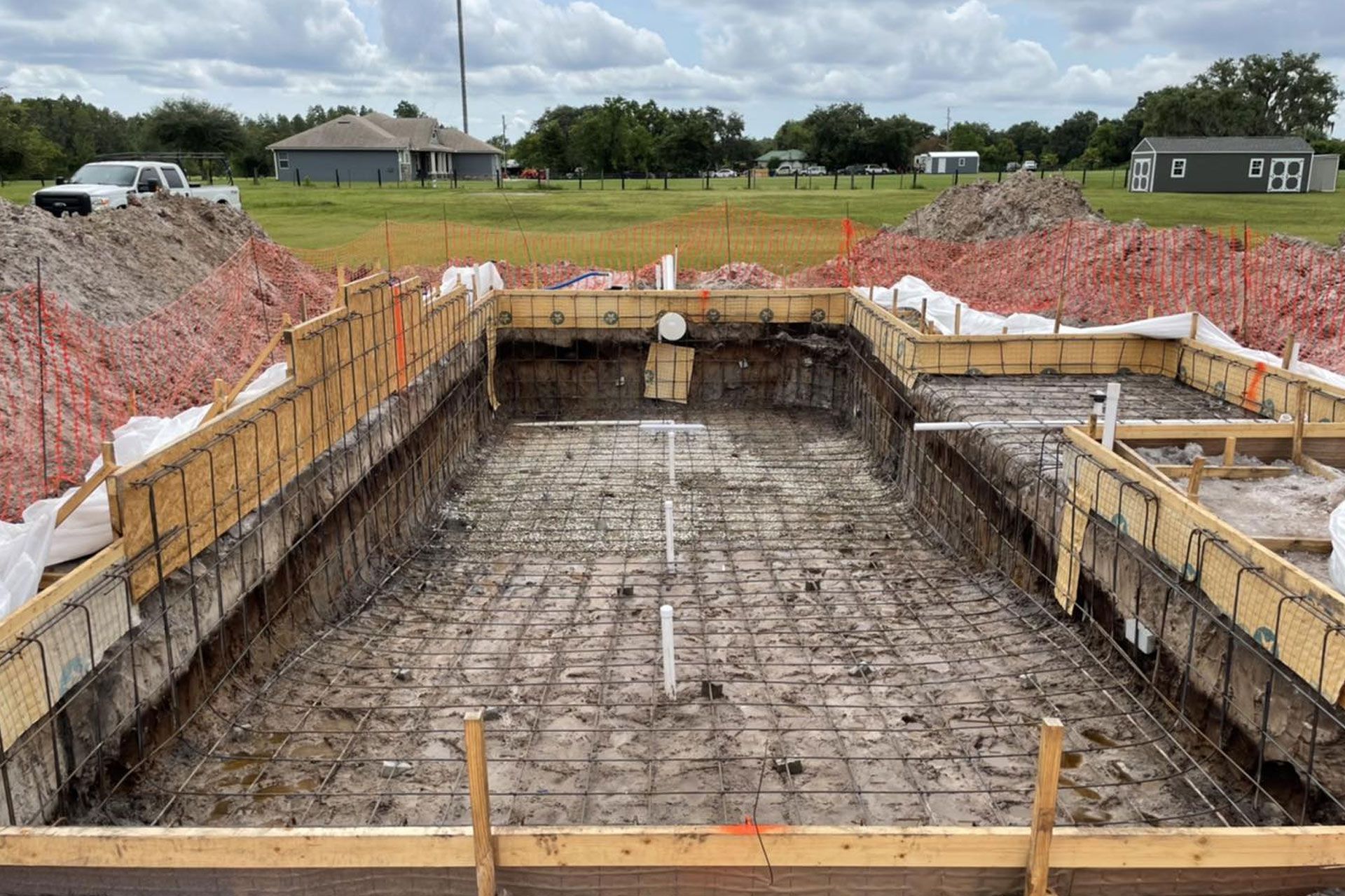 Pool construction site with wooden forms, rebar, and excavated earth.