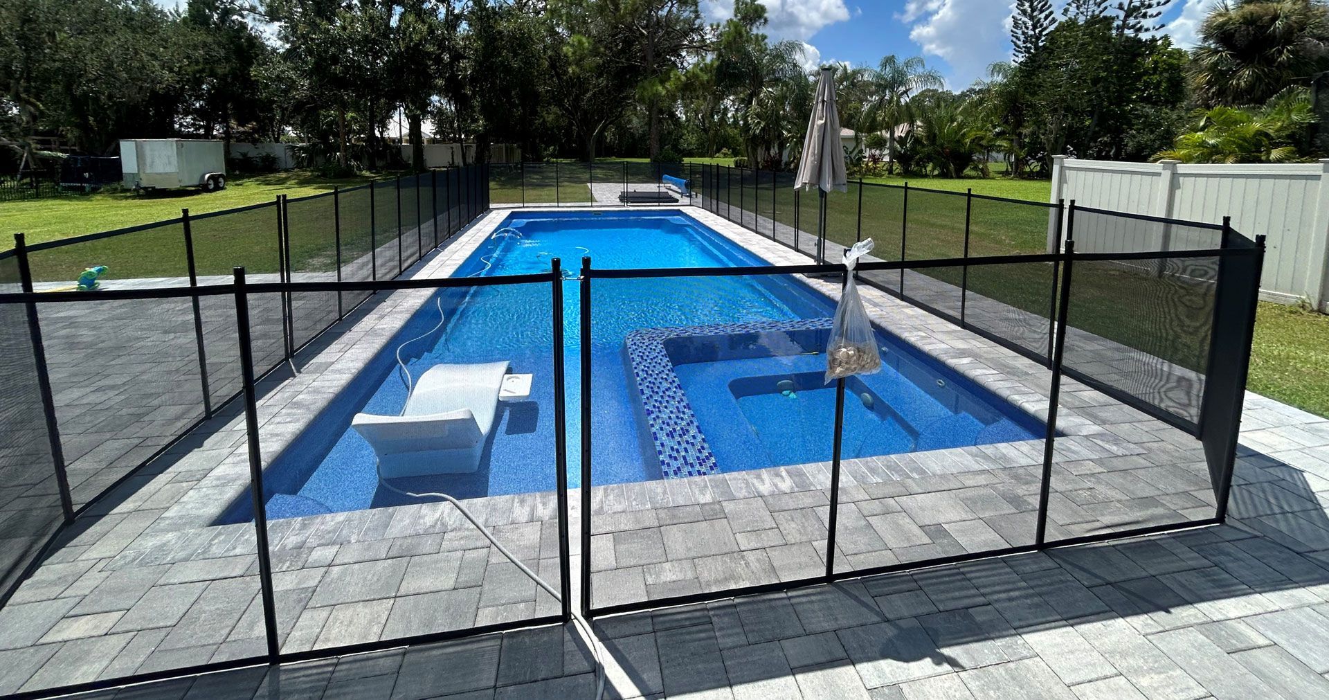 Black mesh safety fence around a blue rectangular swimming pool on a paved patio.
