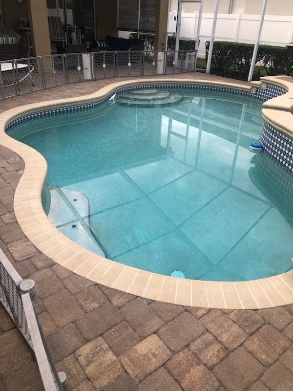 A kidney-shaped swimming pool with blue water and tile surround, set in a paved patio.