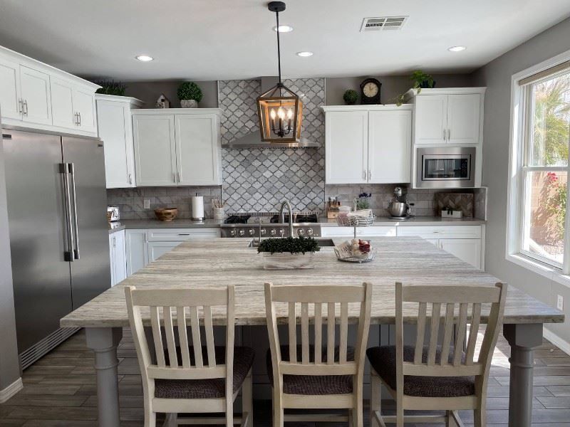 A kitchen with white cabinets , stainless steel appliances , a large island with a table and chairs.