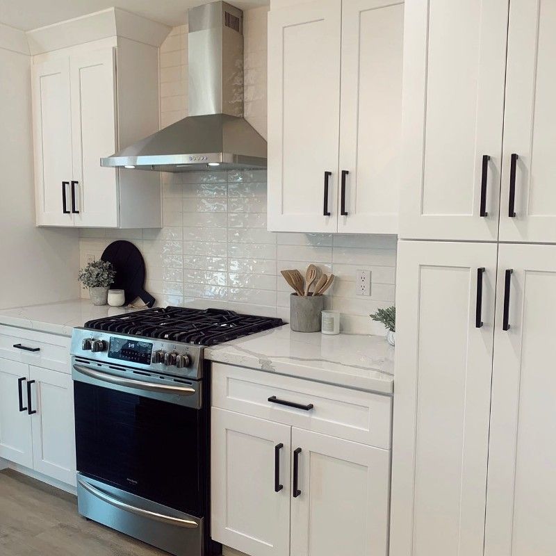 A kitchen with white cabinets , a stove , and a hood.