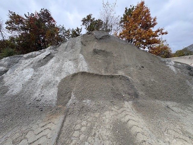 A pile of gray gravel with tire tracks, trees in the background with orange and red leaves.