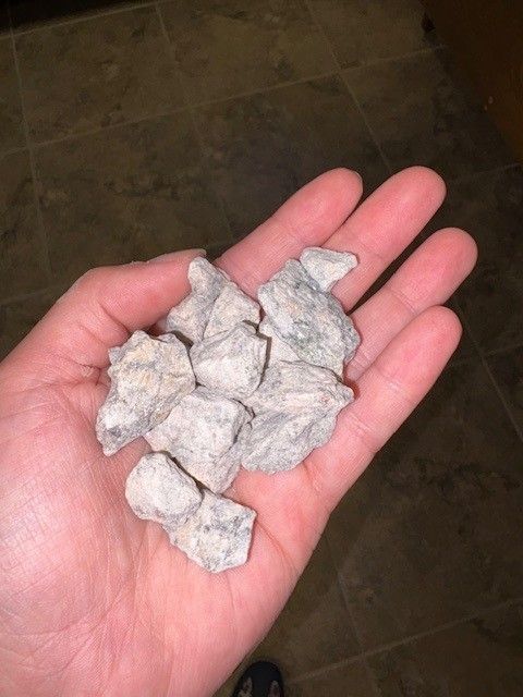 Handful of light-colored, angular rocks held in an open palm. Dark tile floor in background.