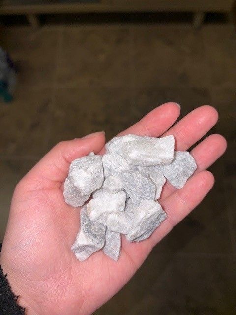 Hand holding a pile of small, light-colored, irregularly shaped rocks.