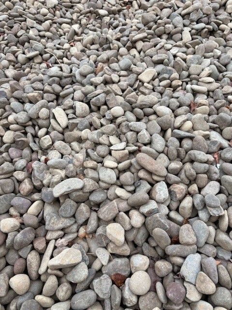 Pile of smooth, gray and tan river rocks, covering the ground.