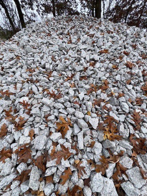 Pile of light gray gravel with scattered brown leaves in a forest setting.