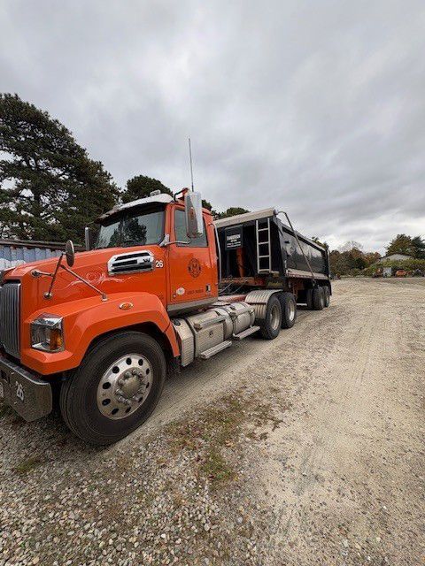 Orange dump truck parked on gravel, under a cloudy sky.