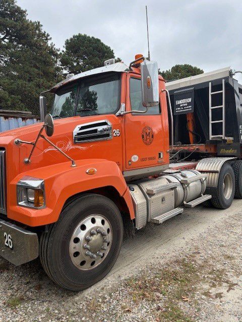 Orange semi-truck with a black trailer. The truck is parked outdoors on a gravel area.